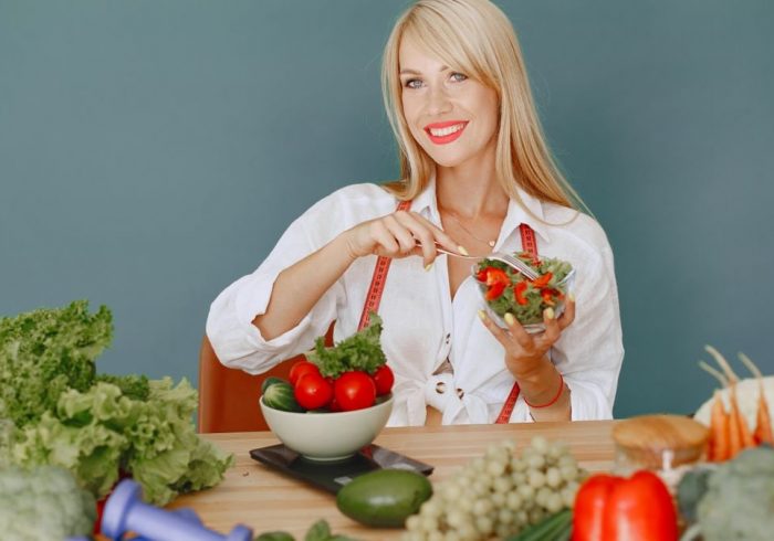 Blonde woman enjoying a fresh salad surrounded by vegetables, promoting healthy eating.